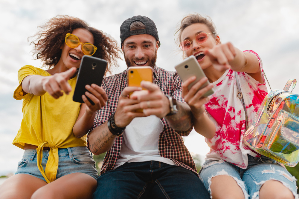 Jovens felizes em companhia de amigos sorridente sentados no parque usando smartphones.